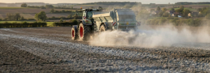 Tracteur avec épandeur réalisant un chaulage agricole, épandage d’amendement calcaire sur chaume avec léger nuage de poussière.