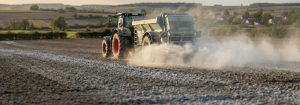 Tracteur avec épandeur réalisant un chaulage agricole, épandage d’amendement calcaire sur chaume avec léger nuage de poussière.