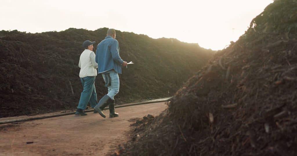 Deux personnes marchent entre les andains d'une plateforme de compostage